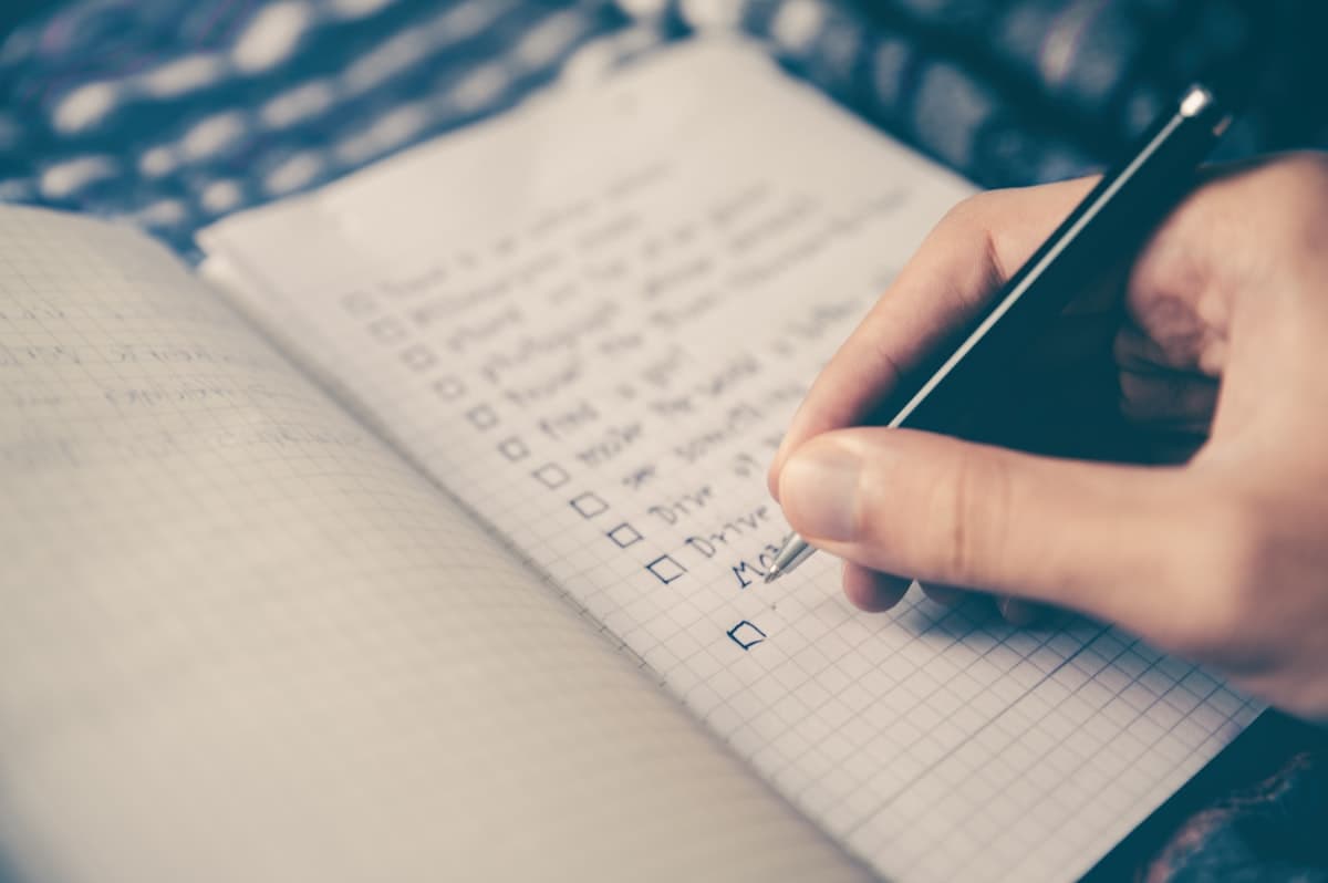Seseorang menulis daftar checklist dengan pulpen di atas buku catatan.