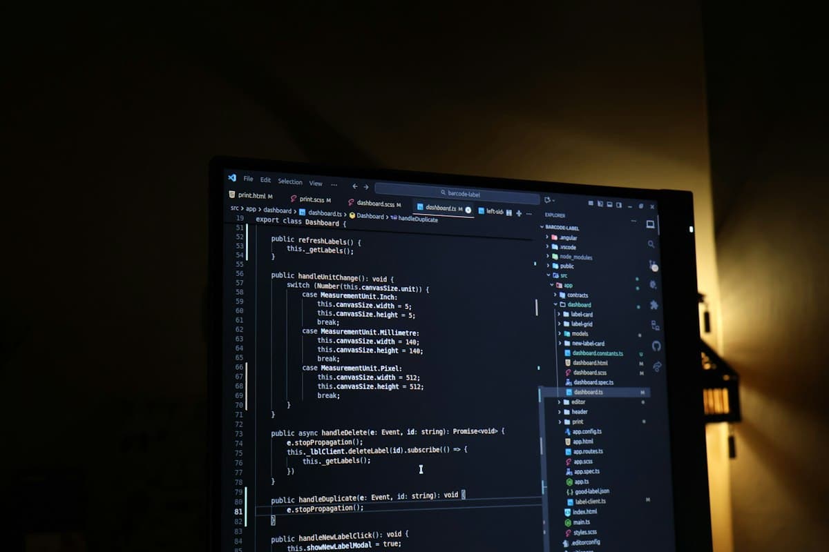 Layar monitor menampilkan baris-baris kode editor mode gelap dengan pencahayaan kuning hangat di latar belakang.