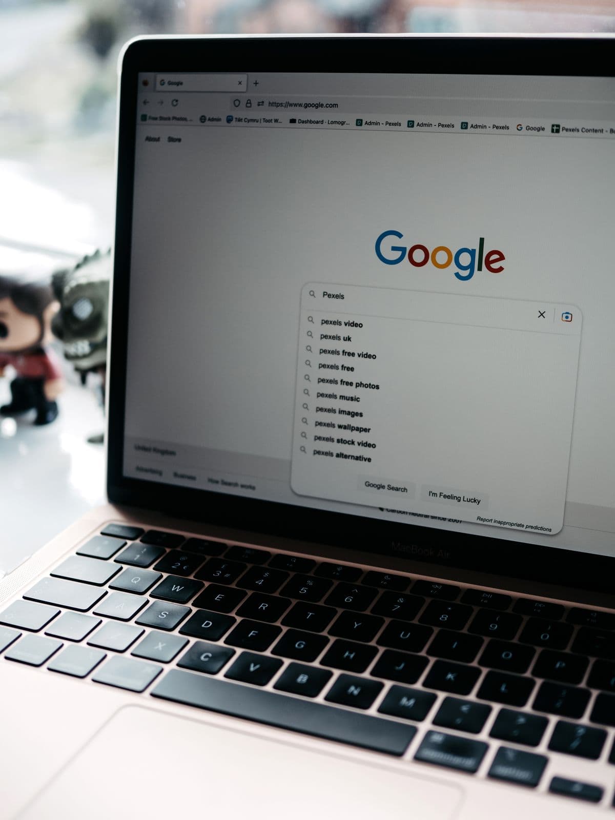 Layar laptop menampilkan halaman utama Google dengan kolom pencarian dan saran autocomplete.