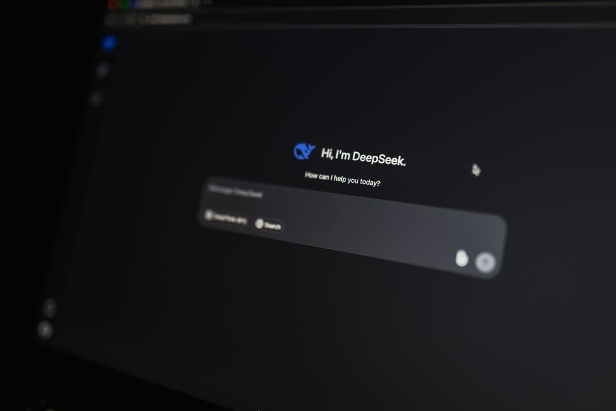 Layar laptop menampilkan antarmuka chat AI dengan sapaan 'Hi, I'm DeepSeek. How can I help you today?' dan kolom input pesan di bawahnya.