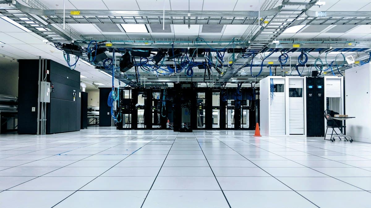 Rak server data center berjajar dengan kabel jaringan biru melintang di langit-langit.
