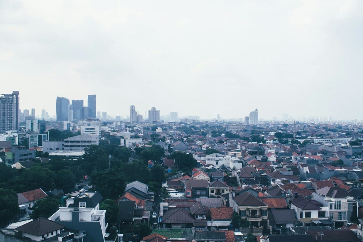 Pemandangan udara kota Jakarta dengan gedung pencakar langit di kejauhan dan atap rumah padat di latar depan.