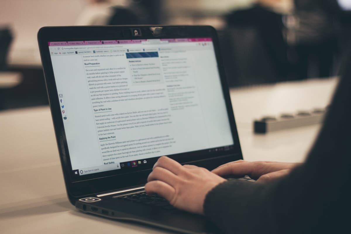 Tangan mengetik di keyboard laptop dengan layar menampilkan artikel blog dan daftar 'Related Articles' di sisi kanan.