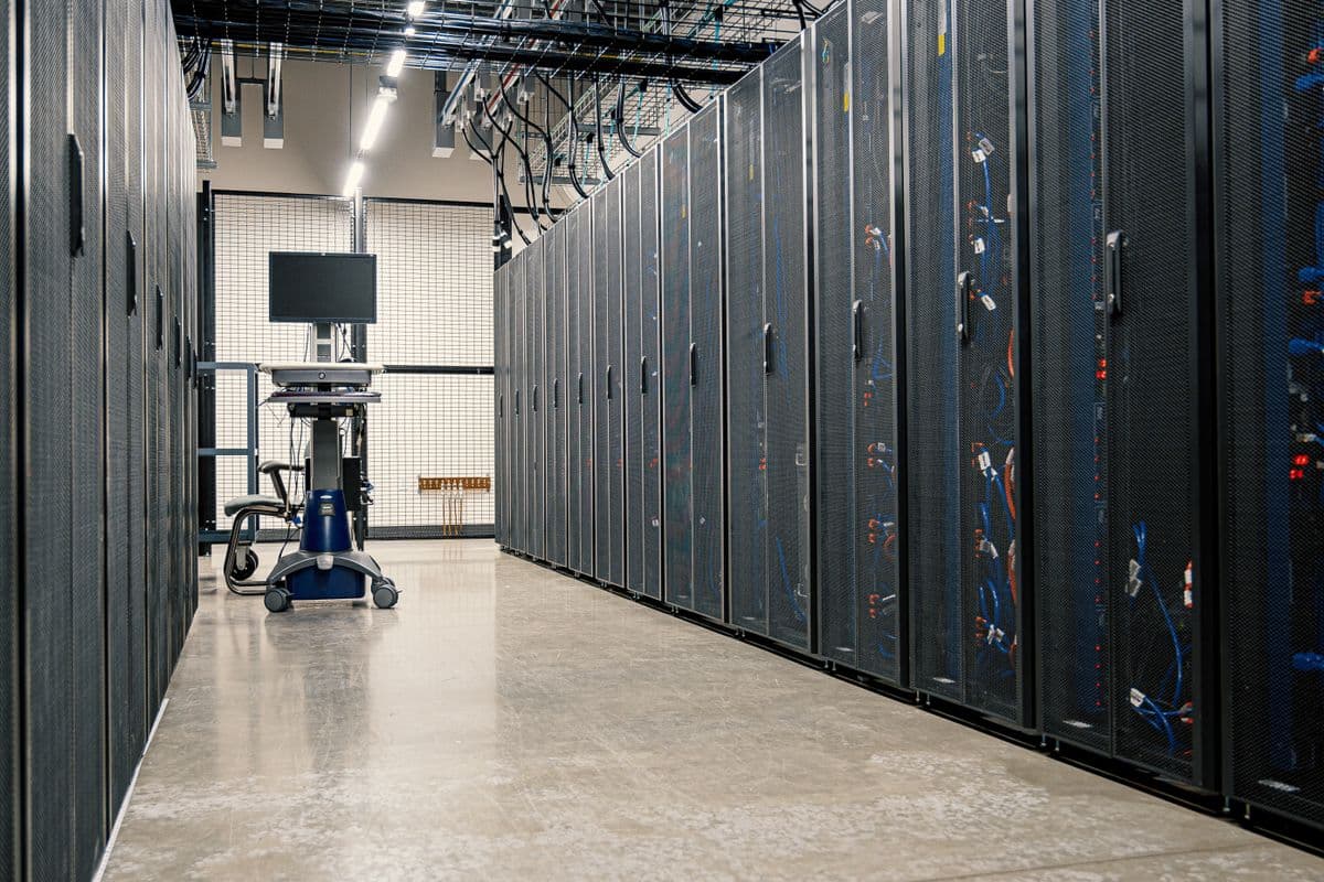 Rak server data center dengan lampu indikator biru menyala di ruangan gelap.