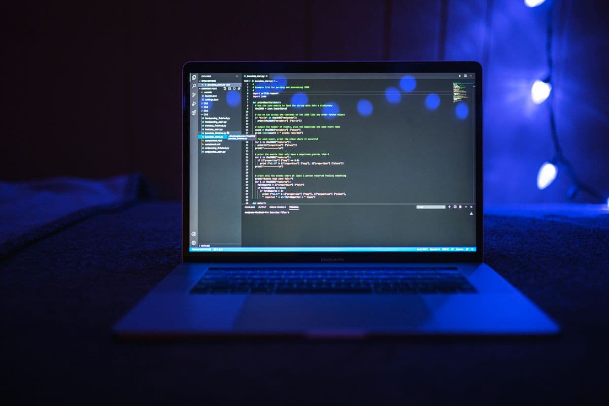 Layar laptop menampilkan kode dengan pencahayaan biru gelap, close-up dari samping.