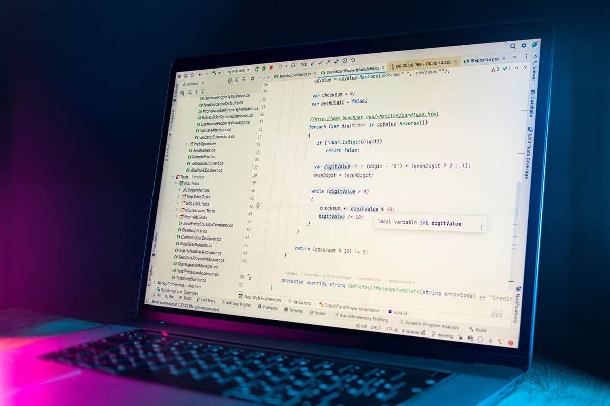 Layar laptop menampilkan kode editor dengan syntax highlighting warna-warni di ruang kerja.