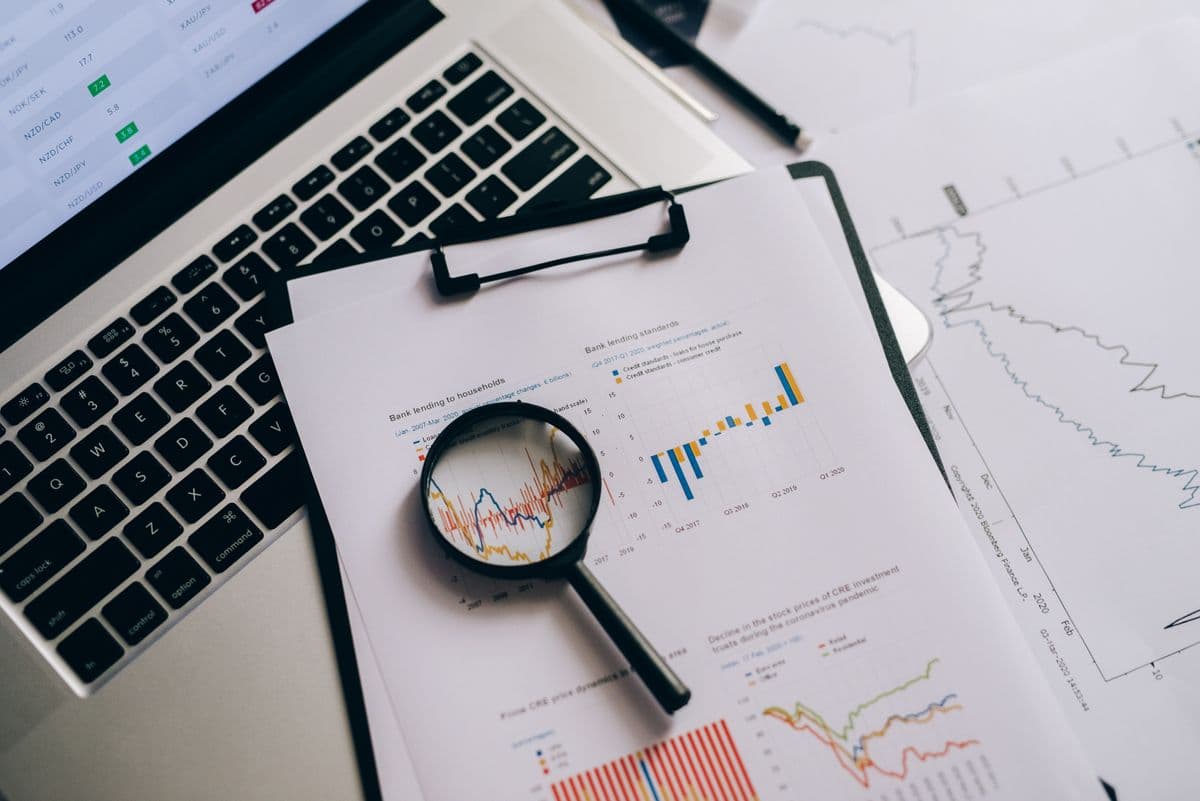 Kaca pembesar di atas kertas berisi grafik dan data statistik di meja kerja.